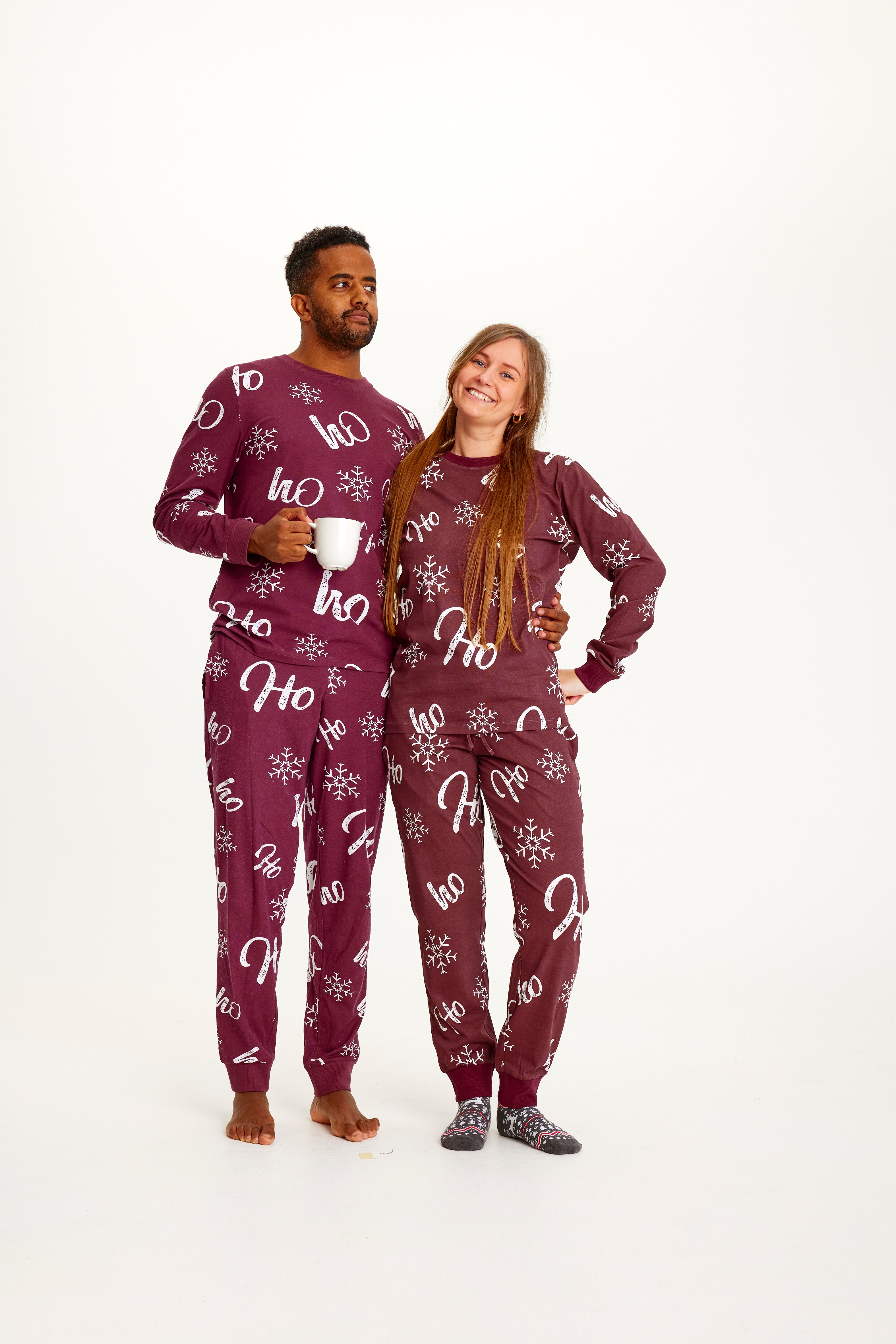 Poserende mann og kvinne iført rød julepyjamas med julemønster.